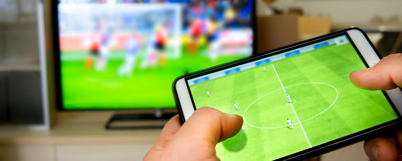 Person interacting with a soccer game on a mobile device while watching a game on TV