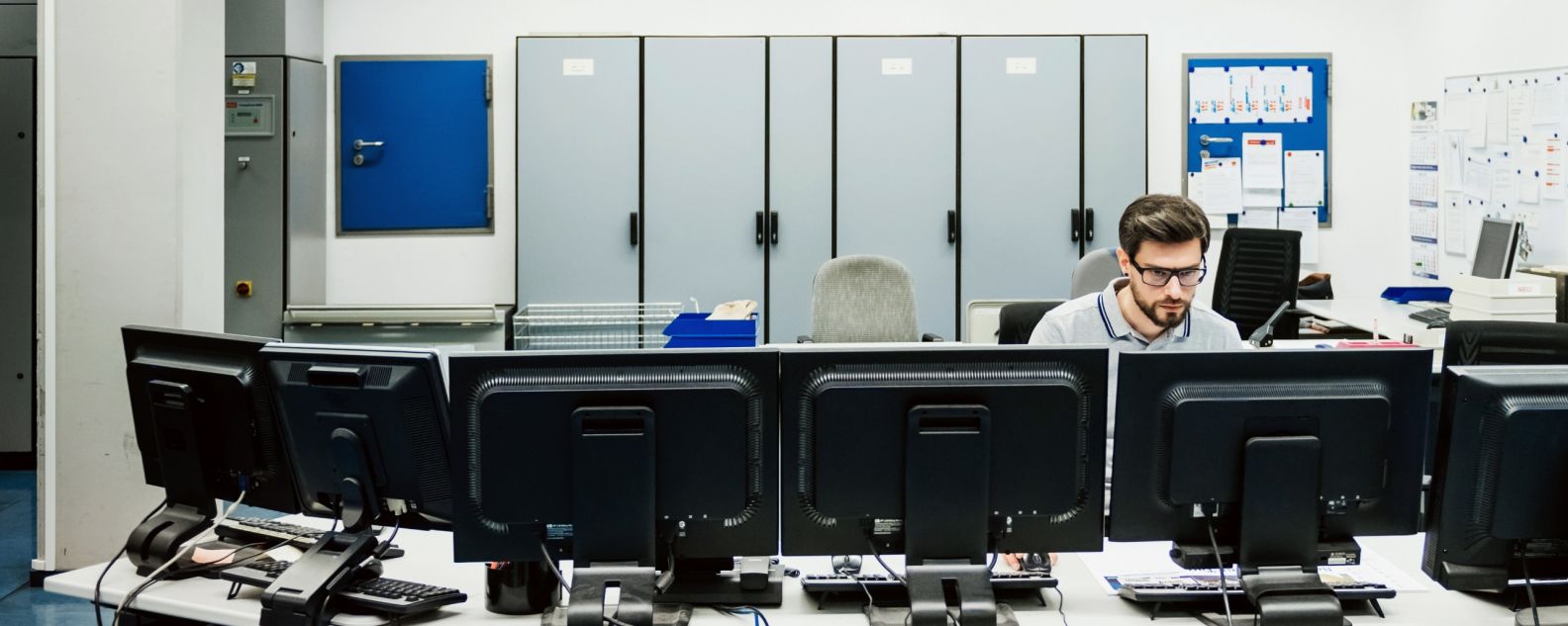 Une personne assise derrière une rangée d’ordinateurs de bureau
